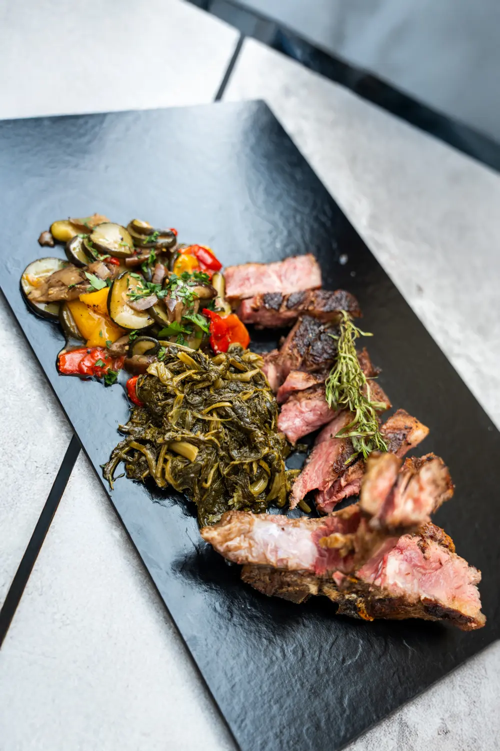 Ein Tellergericht mit einem Steak, sautiertem Gemüse und etwas, das wie Blattgemüse aussieht, möglicherweise Spinat oder ein ähnliches gekochtes Gemüse. Von Nicchia GmbH