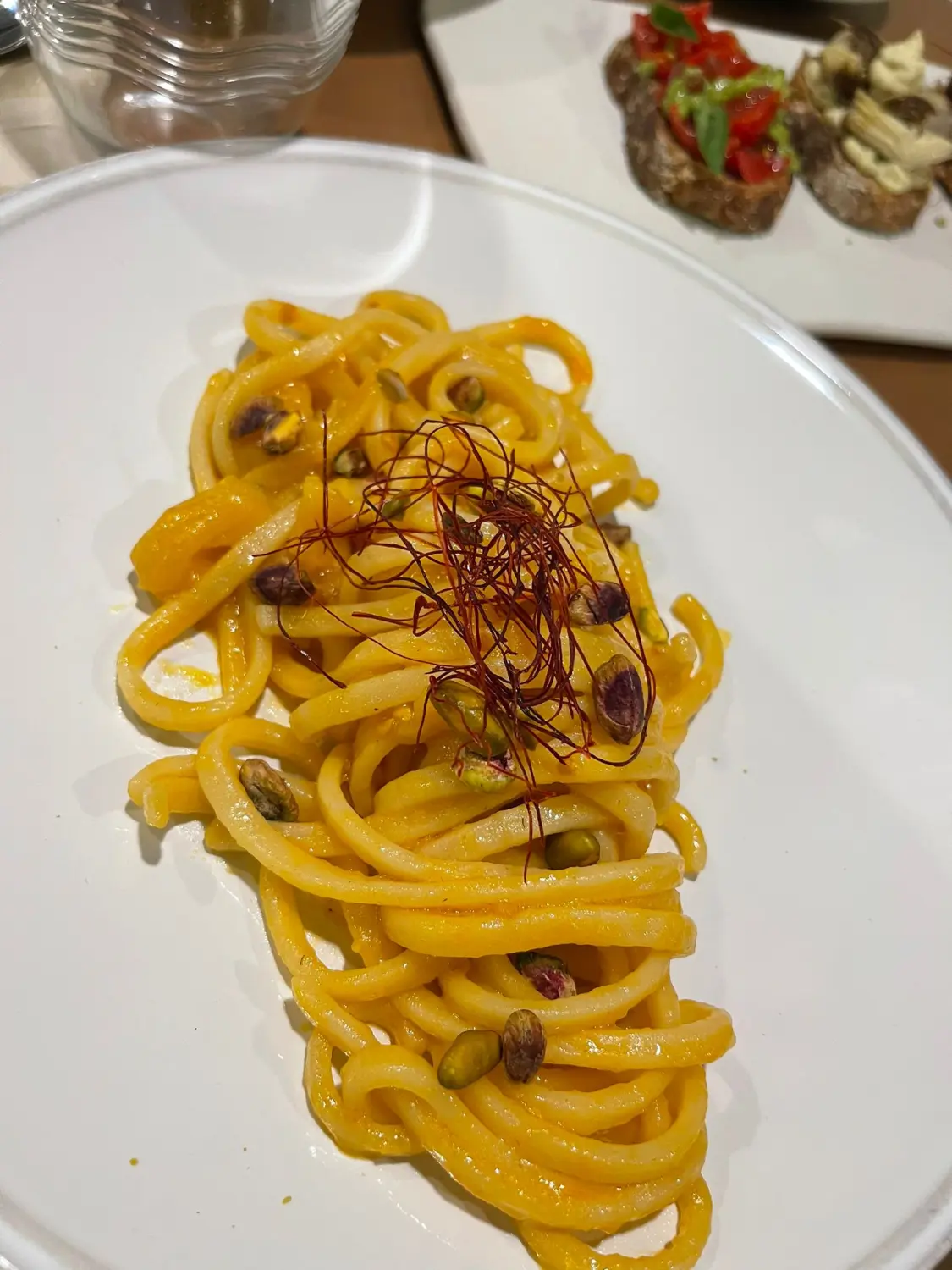 Ein Teller Spaghetti mit gelb-oranger Sauce, garniert mit Pistazien und etwas, das wie Safran- oder Chilifäden aussieht. Von Nicchia GmbH